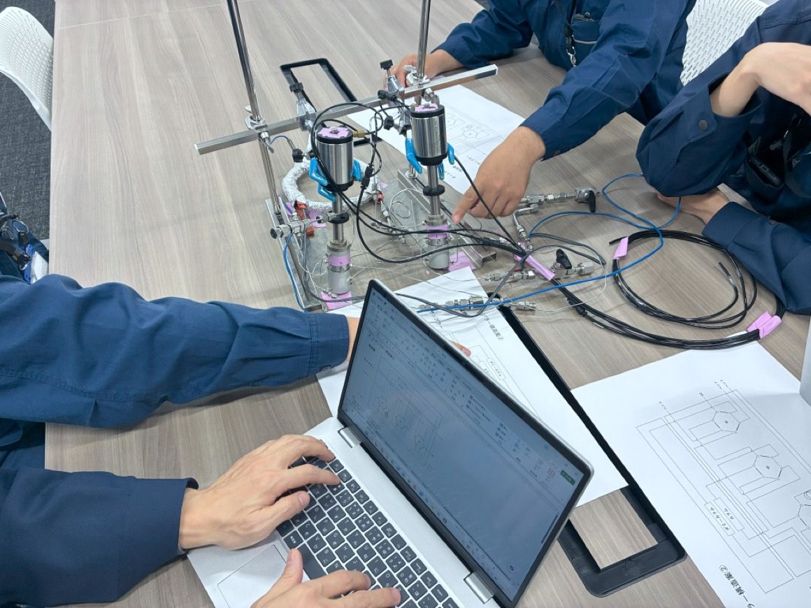 実験装置とノートパソコンを前に打ち合わせする研究員の様子